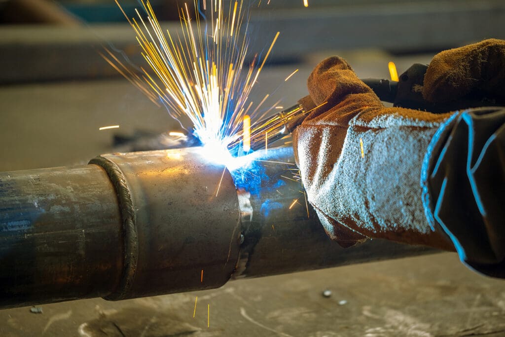 A closeup of a person welding a metal pipe, wearing safety gloves.